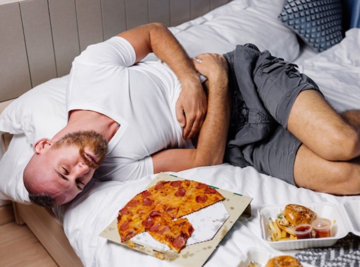 Uomo mangia la pizza a letto